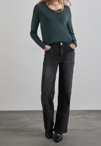 Mörkgrön stickad tröja med v-ringning och ribbade muddar, kombinerat med högmidjade, vida svarta jeans och svarta klackstövlar.