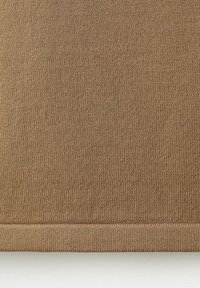 Gros plan sur un tissu tricoté brun clair avec une texture fine côtelée et un ourlet soigneusement fini au bord inférieur.
