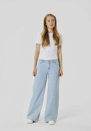 Jean large bleu clair en denim, associé à un t-shirt blanc ajusté. Les jeans disposent d'une fermeture à boutons et de poches latérales.