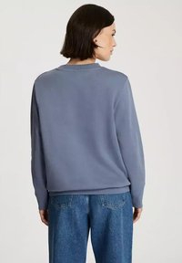 Niebieski sweter, okrągły dekolt, długie rękawy, miękka tekstura, luźny krój, w połączeniu z luźnymi niebieskimi dżinsami z tylnymi kieszeniami i subtelnymi detalami przeszyci.