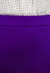 Gros plan d'un tissu en maille blanche avec de petites perles brillantes associé à un tissu violet uni en dessous.