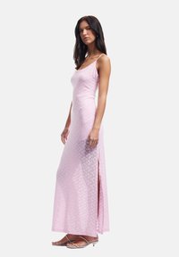 Robe maxi rose avec une silhouette cintrée, texture en dentelle et fente sur le côté. Comprend des bretelles fines en spaghetti et un motif floral subtil.