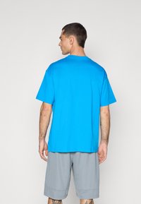 Kreminis T-shirt ryškiai mėlynos spalvos, pagamintas iš medvilnės, trumpomis rankovėmis, laisva forma. Derinamas su šviesiai pilkais sportiniais šortais, minimalus matomas detalizavimas.
