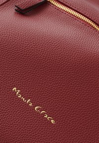 Sac en cuir texturé rouge avec fermeture éclair dorée et logo embossé "Manila Grace" dans le coin inférieur gauche.