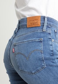 Blå denimjeans med hög midja, med en läderlapp märkt "Levi Strauss & Co." och bakfickor med böjda sömdetaljer.