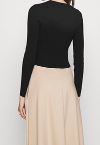 Maglietta nera a maniche lunghe con un design aderente, scollatura rotonda e orlo corto, abbinata a una gonna beige fluida.