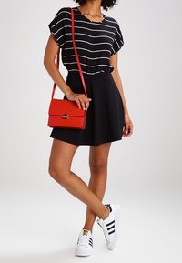 Svart och vit randig kortärmad topp, svart kjol, vita sneakers med svarta ränder, röd axelväska. Enkel, avslappnad outfit.