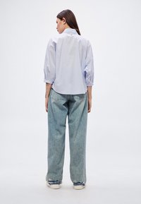 Ανοιχτό μπλε πουκάμισο με κοντά μανίκια και κολάρο στο πίσω μέρος, συνδυασμένο με άνετο, φθαρμένο τζιν σε ανοιχτό χρώμα και λευκά αθλητικά παπούτσια. Καθημερινή εφαρμογή και στυλ.