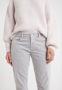 Pantalones de corduroy slim-fit en gris claro con una textura sutil y cierre de botón. Combinados con un suave suéter de punto acanalado en rosa claro.
