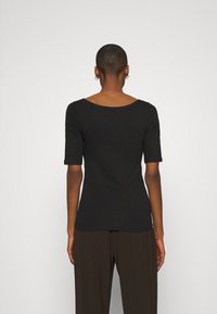 Svart kortärmad topp med rund halsringning och figurnära design. Bakifrån syns en jämn textur och lätt stretchmaterial.