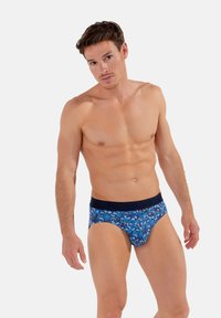 Blaue gemusterte Shorts mit einem marineblauen Elastikbund. Das Design weist komplexe Formen und Texturen auf und besteht aus weichem Material für zusätzlichen Komfort.