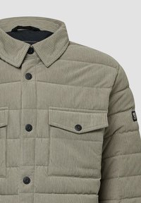 Lichtgrijs corduroy jack met een gewatteerd ontwerp, twee borstzakken, zwarte knopen en een spread kraag. Geweven stof met verticale ribbels.