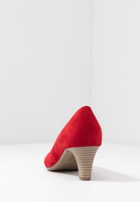 Chaussure à talon haut en suède rouge avec une pointe pointue et un talon cylindrique texturé. Fini lisse sans motifs ou accents visibles.
