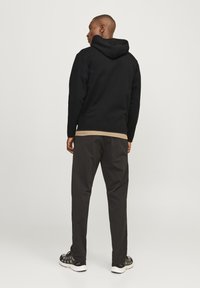 Svart hoodie med avslappet passform, kombinert med mørke, innsnevrede bukser. Glatt tekstur og minimalistisk design, passende for uformell bruk.