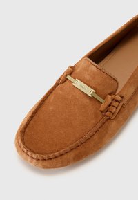 Suede loafers in light brown with a stitched design. Features a gold-tone metal accent bar with "BOSS" engraving. Smooth interior lining.