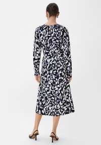 Vestido negro de manga larga con un patrón abstracto en blanco y azul, con un corte holgado y una longitud hasta la mitad de la pantorrilla. Tela suave y elástica.