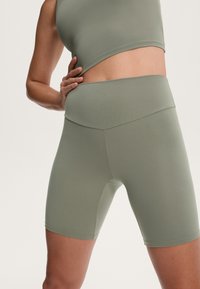 Höga, olivgröna sportshorts tillverkade av ett mjukt, stretchigt material, utan synliga sömmar och med en åtsittande design för komfort.