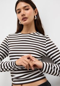 Långärmad topp med horisontella bruna och vita ränder, lättviktstyg, figurnära design, rund halsringning och slät textur.
