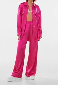 Pink satin oversized shirt paired with matching wide-leg pants. The outfit features a smooth texture, button closures, and elastic waistband.