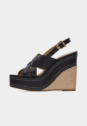 Schwarze Keilsandalette aus Leder mit geflochtenem Jutefußbett, gekreuzten Riemen und goldfarbener Schnalle mit Initialen am Knöchelriemen.