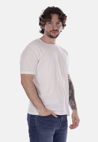 T-shirt rosa chiaro a maniche corte realizzato in cotone morbido con scollatura a girocollo classica, abbinato a jeans blu. Design semplice e privo di decorazioni.