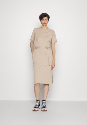 Vestido de algodão bege com mangas curtas, cintura cintada, bolsos laterais e comprimento até ao joelho. Combinado com sapatilhas de cano alto em preto e branco.