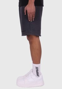 Grå bomuldsshorts med detaljer i sidefald og søm, parret med hvide sneakers og mærkede hvide sokker med sort tekst.