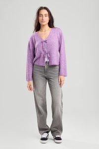 Purple cropped sweater with tie detail at the neckline, paired with gray high-waisted jeans and black sneakers with white laces.