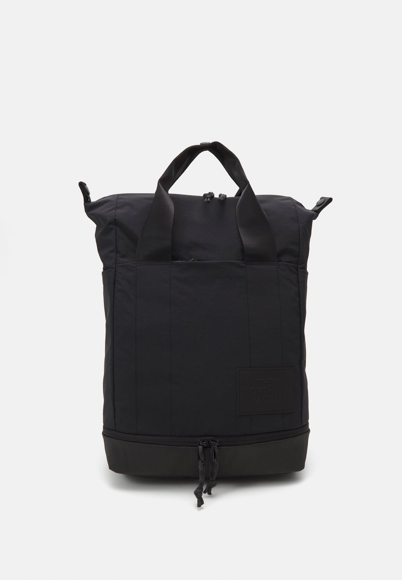 Sac à dos rectangulaire noir avec poignées en haut, doubles fermetures éclair sur les compartiments supérieur et inférieur, et un discret patch avec le logo de la marque au centre avant.