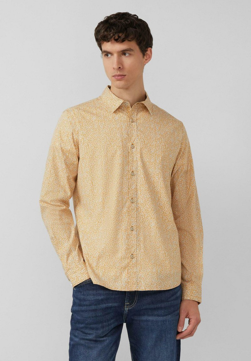 Langarm blouse in gele stof met kleine witte en oranje bloemenprint. Voorzien van een kraag en knopen aan de voorkant.