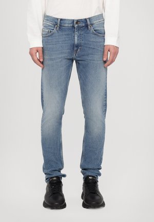 Lichtblauwe denim jeans met een slim fit, voorzien van vijf zakken, een knopenfly en subtiele vervaging. G gedragen met zwarte sportschoenen.