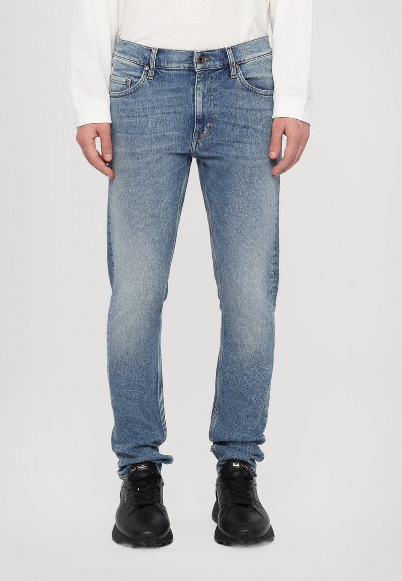 Lichtblauwe denim jeans met een slim fit, voorzien van vijf zakken, een knopenfly en subtiele vervaging. G gedragen met zwarte sportschoenen.