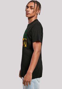 Black cotton t-shirt featuring a multi-color graphic with green, yellow, and red accents, displaying expressive faces in a square pattern.