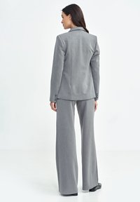 Szary, dopasowany garnitur z taliowanym żakietem i szerokimi spodniami, wykonany z teksturowanej tkaniny z delikatnymi pionowymi paskami i guzikami.
