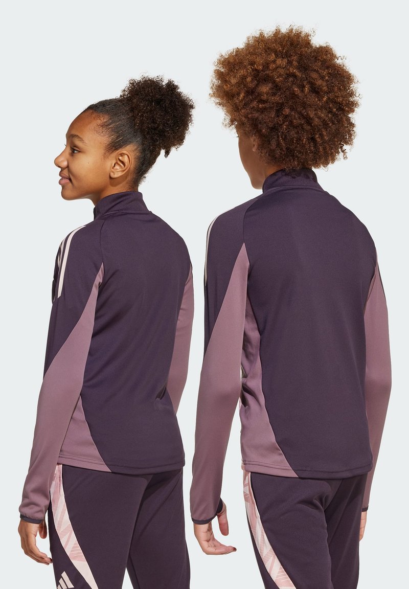 Veste de sport violette avec des accents roses, dotée d'un col haut et de manches longues. Texture lisse avec des panneaux contrastants sur les côtés.