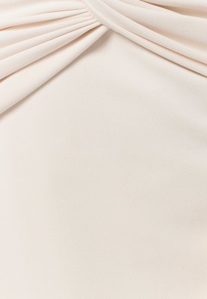 Krēmkrāsas audums ar savītu mezglu augšpusē, rādot gludu, mīkstu tekstūru un smalku austuma rakstu.