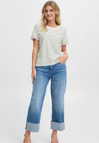 T-shirt à rayures à manches courtes en crème et noir, arborant un logo rouge, associé à un jean en denim à jambes larges avec des ourlets retroussés.