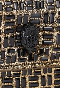 Sac à main noir et or orné, avec une surface texturée présentant des motifs rectangulaires et carrés, surmonté d'un fermoir orné noir.