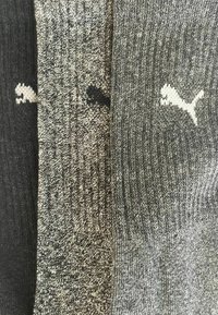 Drei Paar Puma-Socken in Schwarz, Dunkelgrau und Hellgrau, nebeneinander angeordnet, mit sichtbaren Puma-Logos.