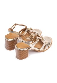 Sandalias de tacón metálico dorado con diseño de tiras cruzadas. Presentan un tacón cuadrado con un acabado de madera texturizada y una plantilla de cuero suave.