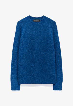 Niebieski sweter z długim rękawem, z okrągłym dekoltem, o puszystej teksturze, z prążkowanymi mankietami i dołem oraz czarną metką marki przy dekolcie.