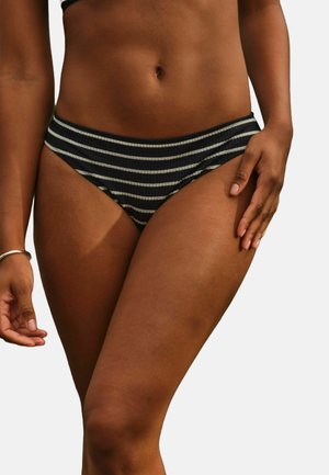 Die Taille und Oberschenkel einer Frau, die schwarze und weiße gestreifte Bikiniunterteile trägt, mit einer Hand, die auf dem Oberschenkel ruht, und einem silbernen Armband am Handgelenk.