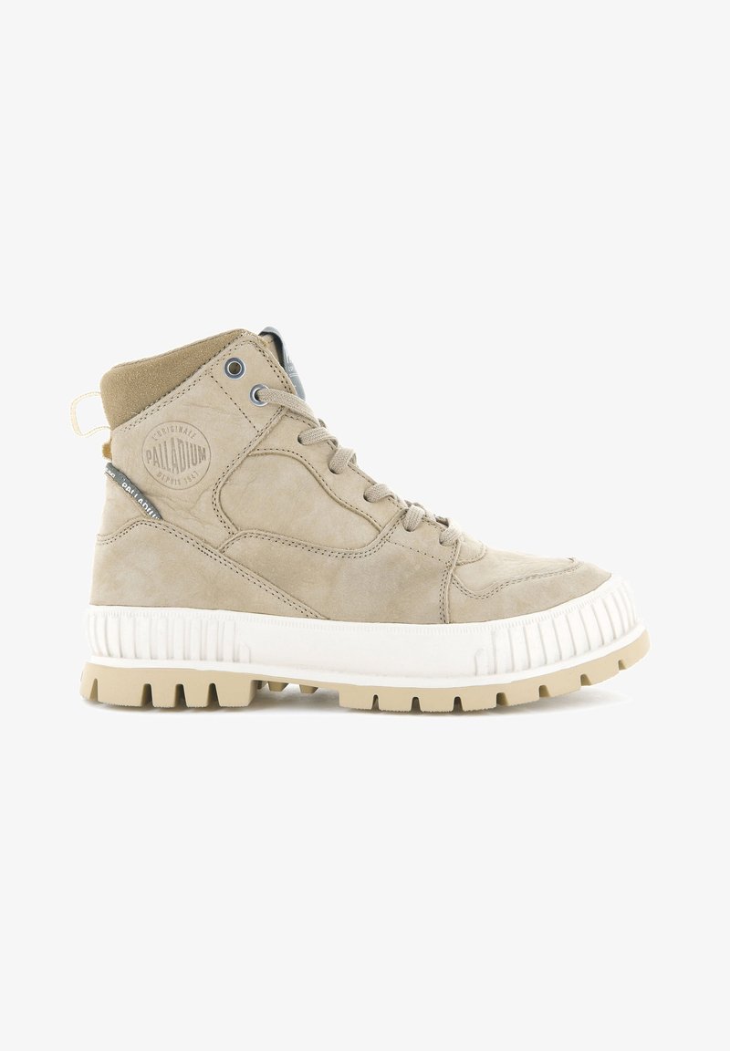 Bottine montante en suède beige avec semelle blanche épaisse, lacets ronds, œillets métalliques et logo Palladium embossé sur le côté.