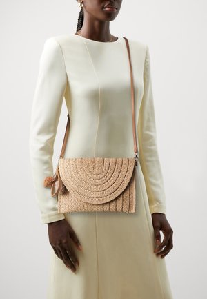 Woven straw crossbody bag in natural beige, featuring a curved flap, horizontal ridges, and a decorative pom-pom on the side.