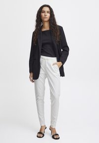 Black blazer over a black top, paired with white tapered trousers. Black strappy high-heeled sandals. Smooth textures throughout.