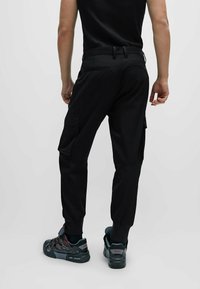 Pantalones cargo negros con un ajuste entallado, cinturilla elástica y múltiples bolsillos. Combinados con zapatillas deportivas negras y rojas.