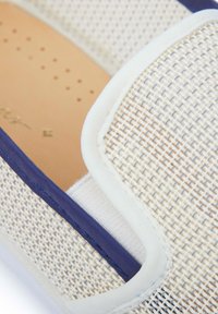 Witte geweven instap schoenen met marineblauwe accenten en een gestructureerd oppervlak. Lichtbruine binnenzool met kleine perforaties voor ademend vermogen.