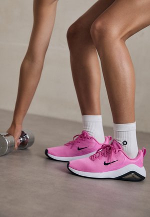 Rosa Nike Sportschuhe mit einem Mesh-Obermaterial, schwarzen Akzenten und einer weißen Sohle, getragen mit weißen Socken, neben einem silbernen Hantel.