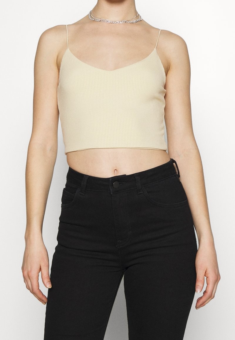 Top corto beige acanalado con tirantes finos y un diseño de escote en V, combinado con jeans negros de tiro alto. Estilo simple y ajustado.