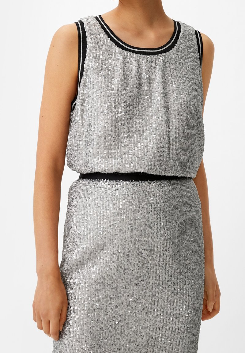 Robe en sequins argentés à design sans manches. Elle présente une bordure noire au niveau du décolleté et de la taille, créant une silhouette ajustée.
